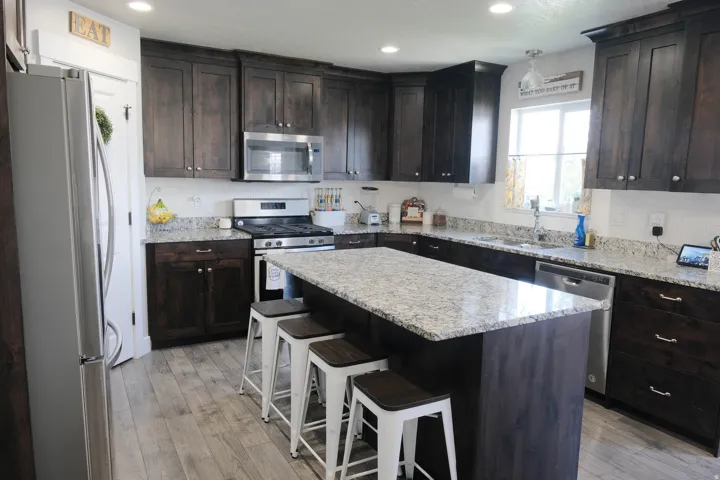 Kitchen featuring dark wood-finish cabinetry, light speckled countertops, a stainless steel gas range, a coordinating dishwasher, and wood-finish flooring