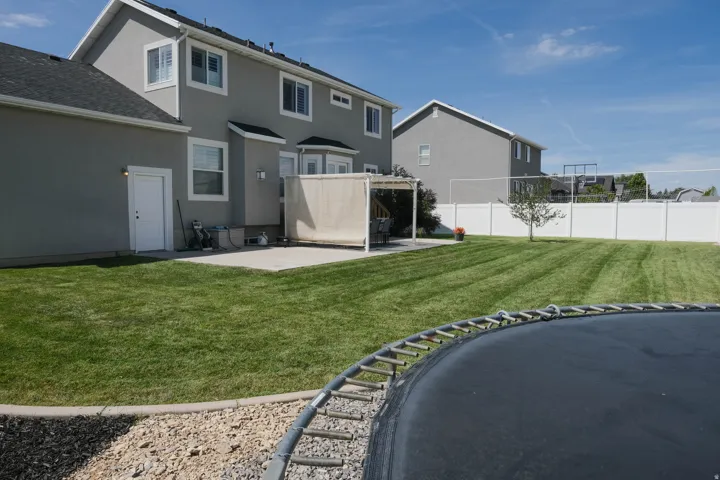 Expansive backyard featuring a manicured lawn, concrete patio, a covered pergola, and privacy fencing