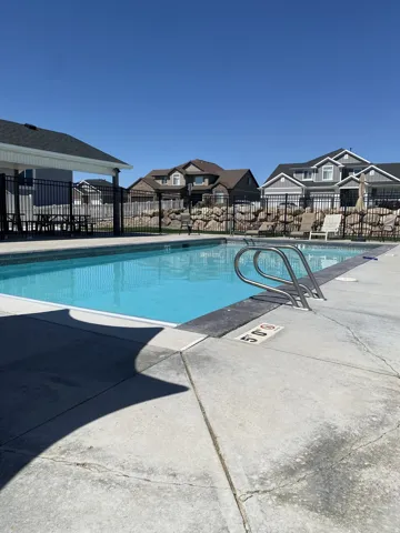 Outdoor swimming pool with concrete surround, metal access rails, and black perimeter fencing