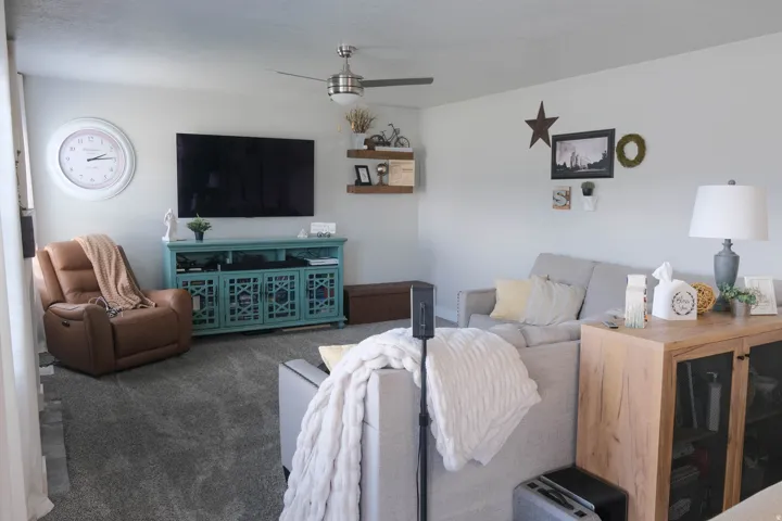 Spacious living area featuring neutral wall tones, ceiling fan, and carpeted flooring