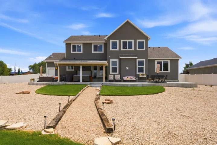 Expansive backyard featuring a covered patio, an additional concrete patio, a gravel landscape, and a manicured lawn area