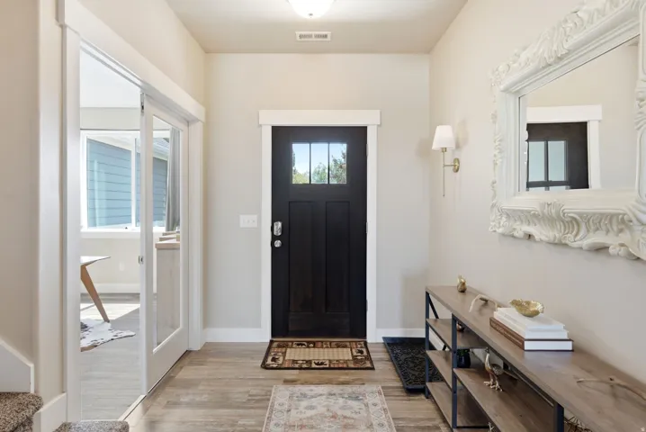 Entryway featuring wood-finish flooring, a dark-paneled front door with clear glass, and a wall sconce