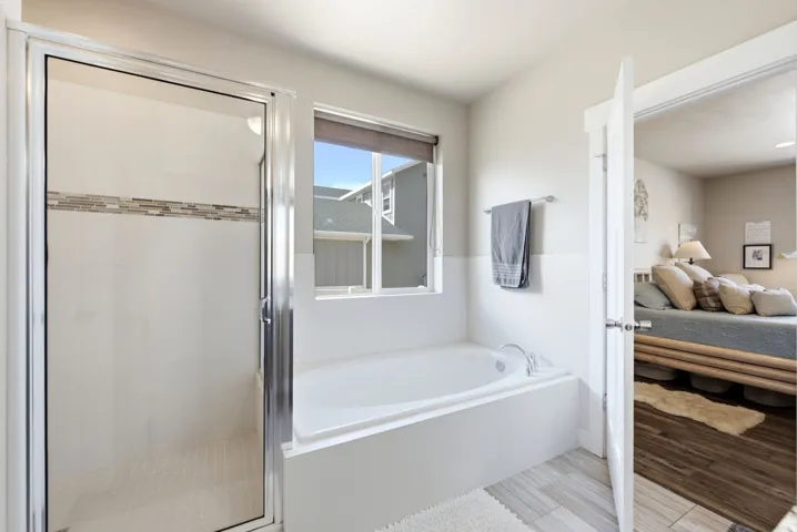 Tiled walk-in shower with a glass door, soaking tub, and a window with roller shade