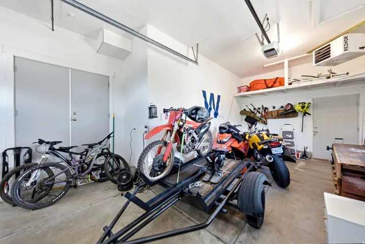 Concrete flooring, overhead shelving, white paneled doors, and a ceiling-mounted garage door opener