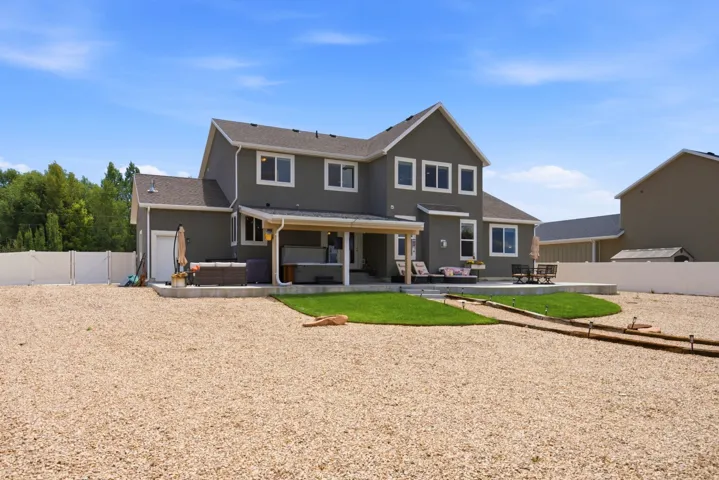 Expansive backyard featuring a covered patio, an additional concrete patio, a manicured lawn, and a gravel-covered area