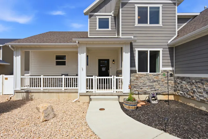 Exterior facade with gray horizontal siding, stone veneer accents, white porch railing, and a covered entry