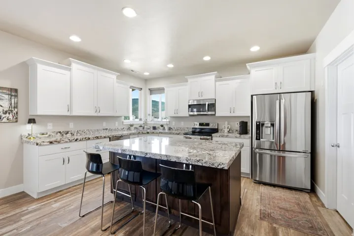 Kitchen featuring white cabinetry, stone countertops, a large island with seating, stainless steel appliances, and wood-finish flooring