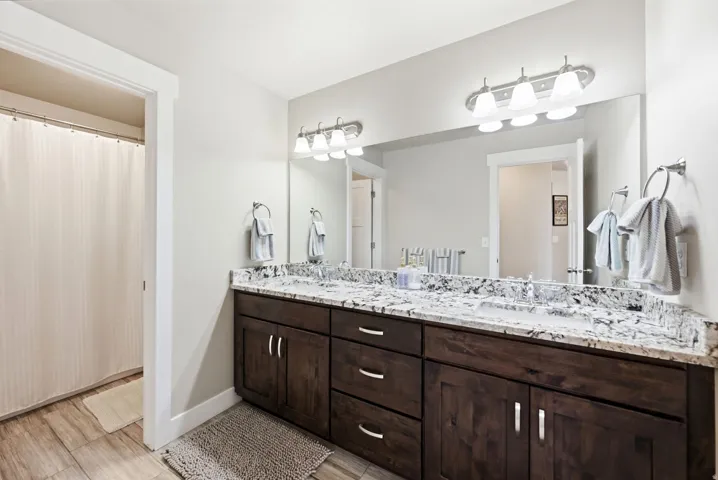 Dual vanity with granite countertop, wood-finish cabinetry, and brushed nickel hardware