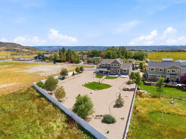 Expansive gravel yard with scattered trees and a defined grassy area, bordered by a white privacy fence