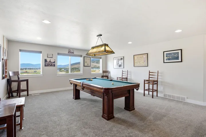 Spacious room featuring light gray carpeting, recessed ceiling lighting, a suspended light fixture, and multiple windows