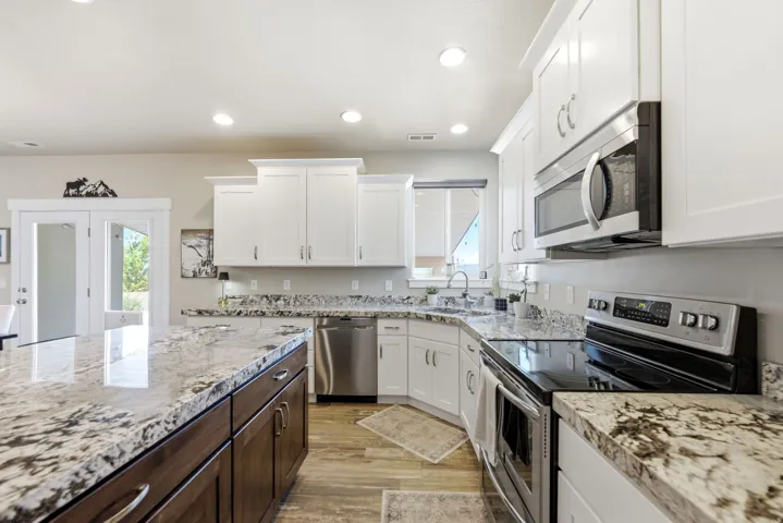 White shaker-style cabinetry, stainless steel appliances, speckled stone countertops, wood-finish flooring, and recessed lighting