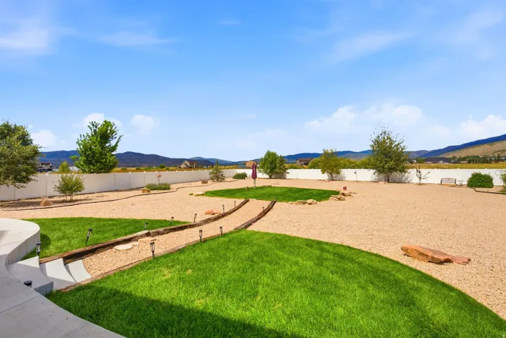 Expansive backyard featuring a white privacy fence, gravel landscaping, and green lawn areas