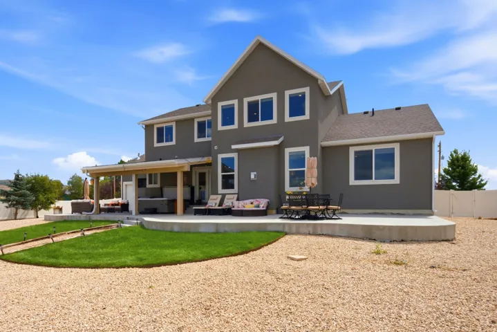 Stucco exterior with multiple windows, covered patio, concrete patio, and a manicured lawn