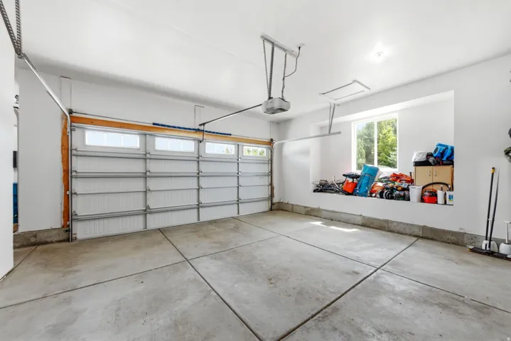 Concrete floor garage with a white sectional door, automatic opener, and a recessed window with an integrated storage ledge