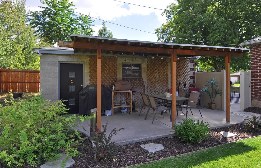 Outdoor patio with a wood-framed pergola, concrete slab, and an adjacent block-constructed storage building