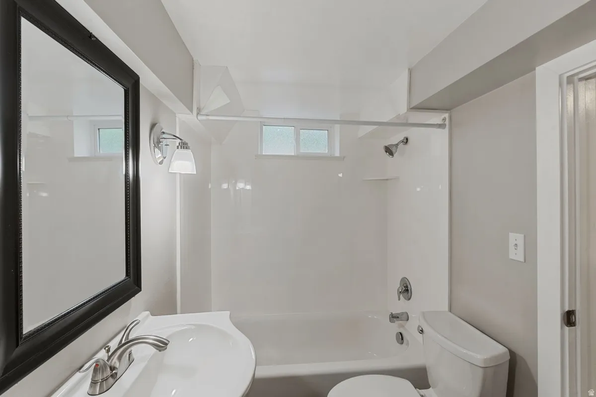 White bathtub with integrated shower, vanity with an undermount sink, framed mirror, and a window