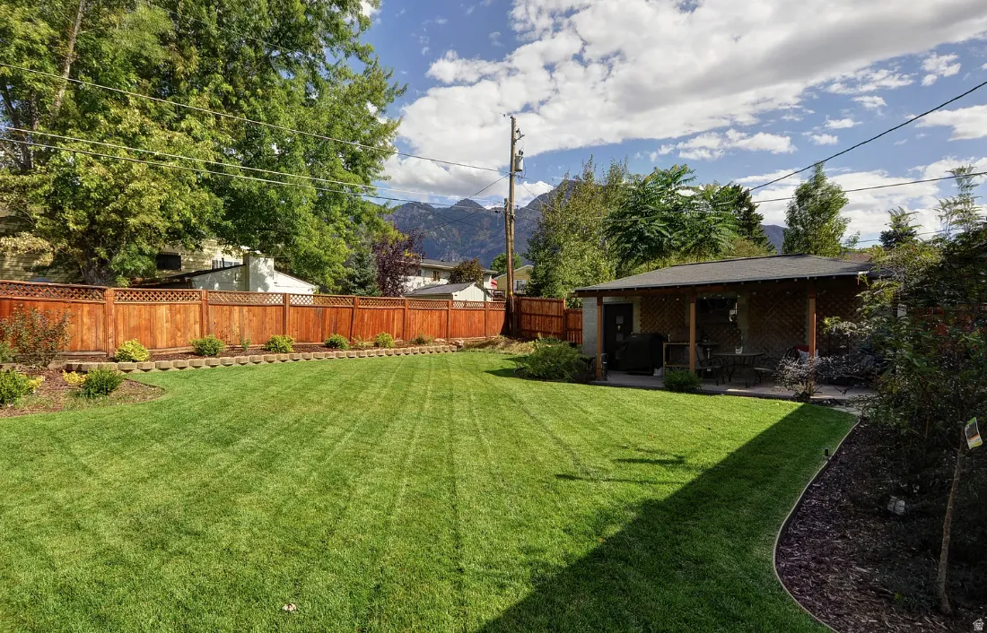 Expansive lawn area with a wood privacy fence, mature trees, mountain backdrop, and a covered patio structure