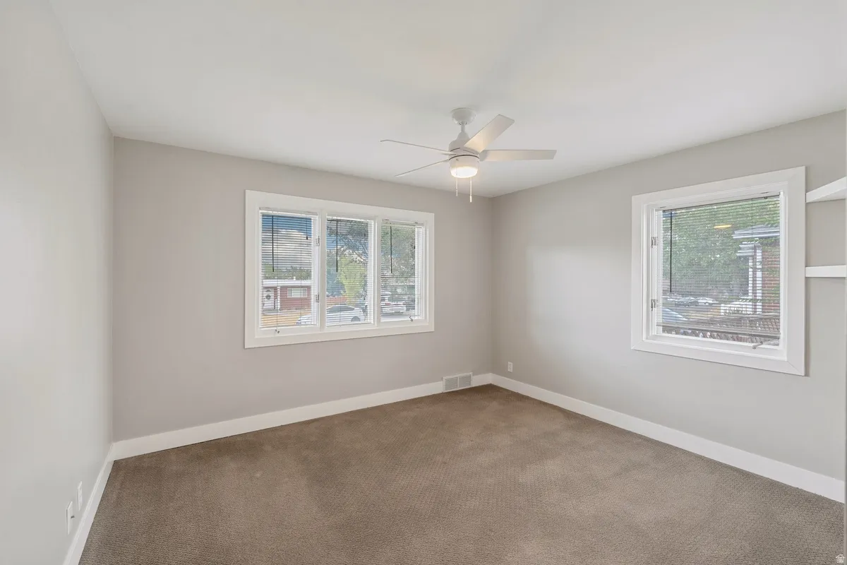 Neutral wall tones, carpeted flooring, multiple windows with white trim, a ceiling fan with integrated lighting, and built-in shelving