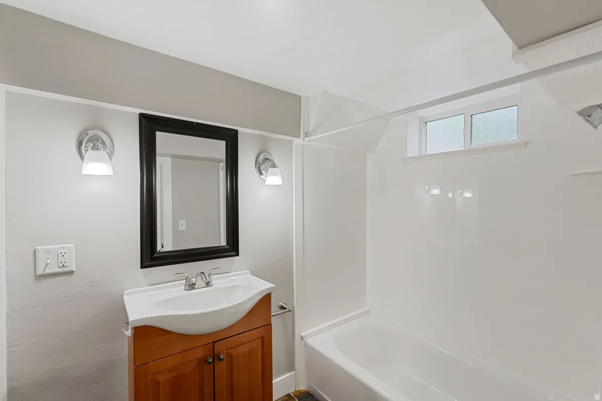 Bathroom featuring a wood-finish vanity with an integrated sink, framed mirror, and chrome wall sconces