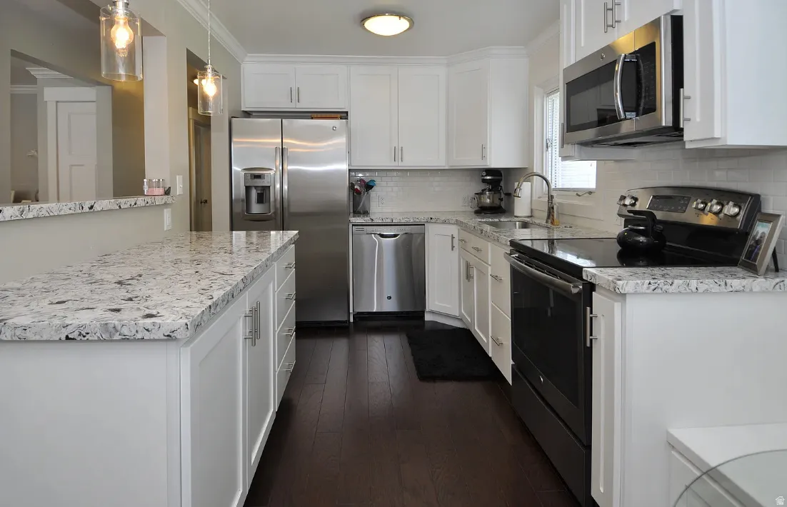 White cabinetry with brushed nickel hardware, stainless steel appliances, speckled stone countertops, a white subway tile backsplash, and dark wood-finish flooring