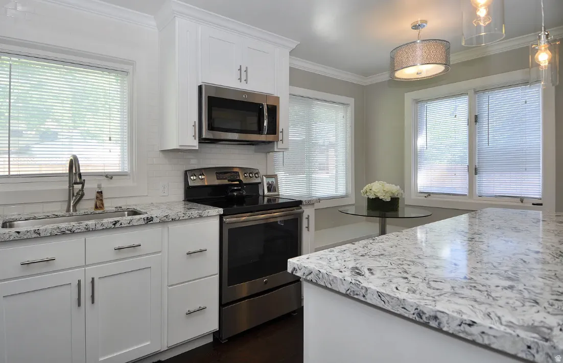 White shaker-style cabinetry with stainless steel hardware, undermount sink with a gooseneck faucet, light-toned patterned countertops, and stainless steel appliances