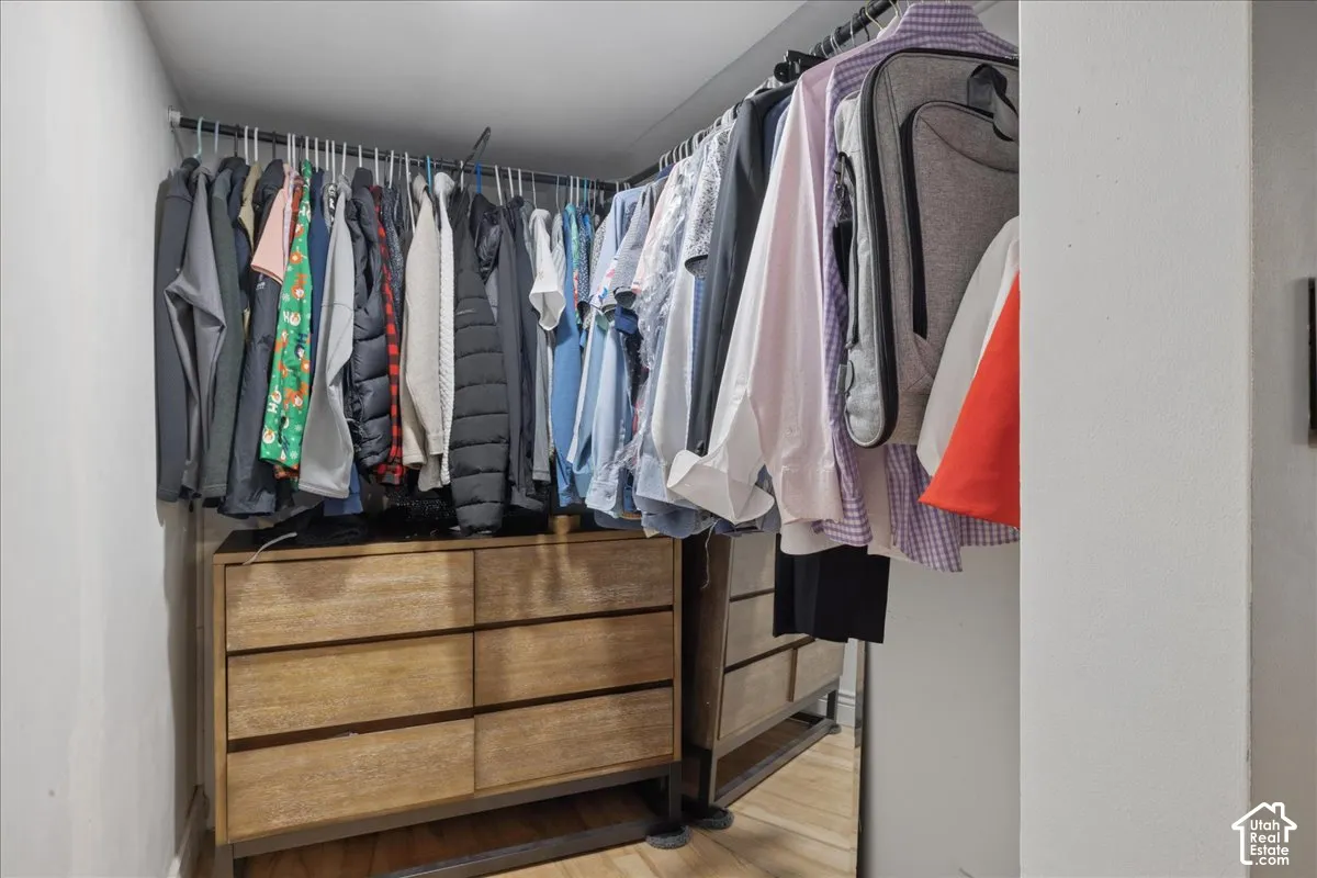 Walk-in closet with integrated wood-finish drawer storage, multiple hanging rods, and a reflective surface