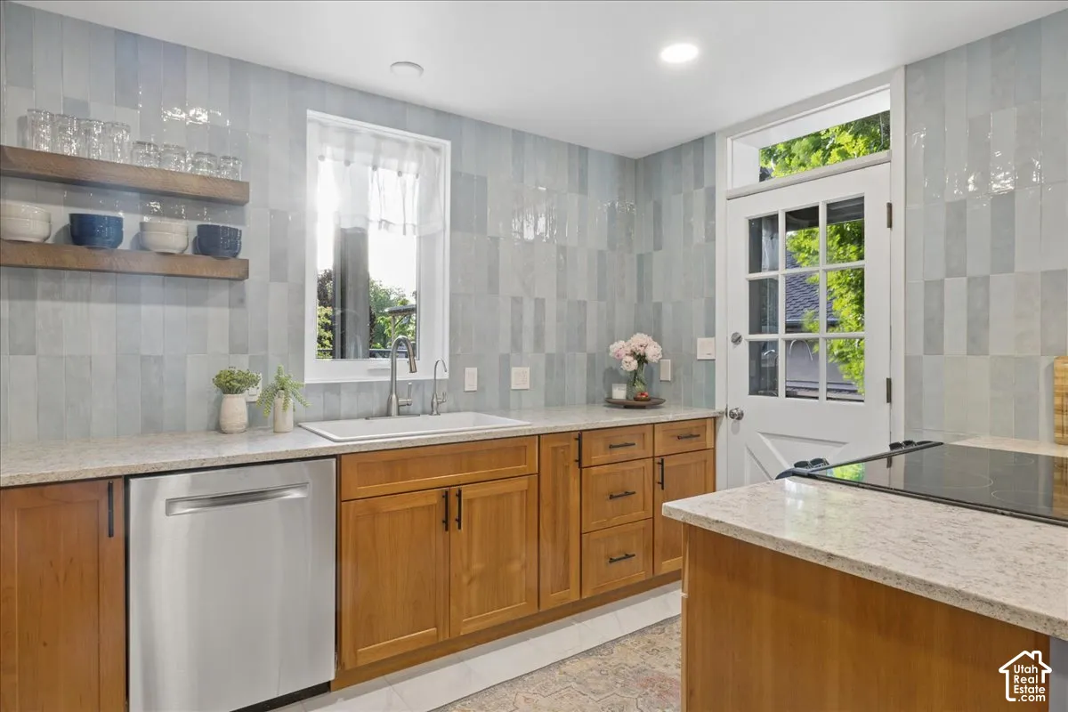Kitchen featuring light wood cabinetry, light-toned countertops, a stainless steel dishwasher, a white single-basin sink with a gooseneck faucet, and light blue subway tile backsplash