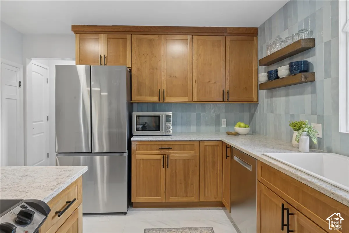 Kitchen featuring wood-finish cabinetry with black hardware, light-toned countertops, a stainless steel French door refrigerator, and an integrated stainless steel dishwasher
