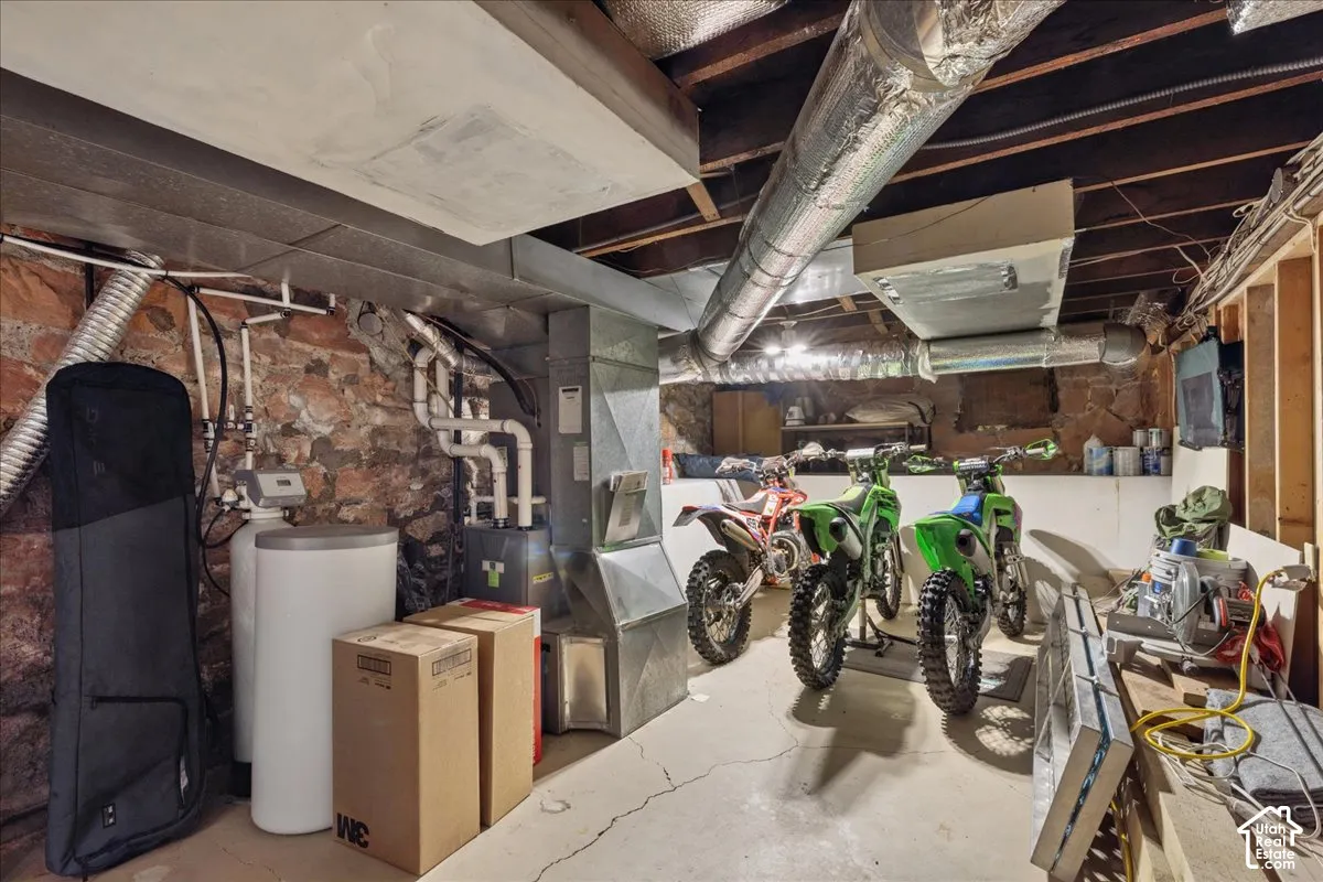 Utility room with exposed stone foundation walls, concrete flooring, and exposed ceiling joists