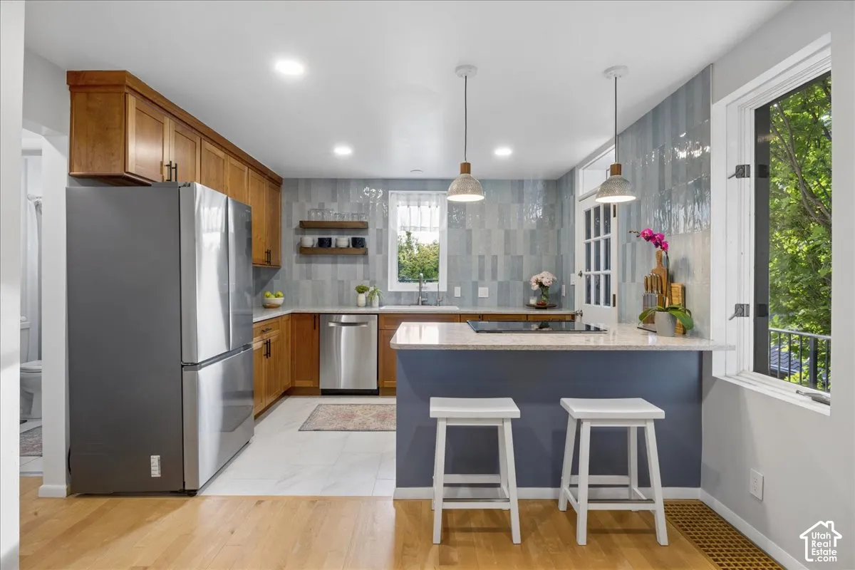 Kitchen featuring wood-finish cabinetry, a central island with countertop seating, light colored countertops, a blue tiled backsplash, and recessed lighting