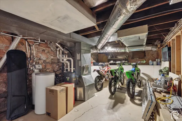 Utility room with exposed stone foundation walls, concrete flooring, and exposed ceiling joists