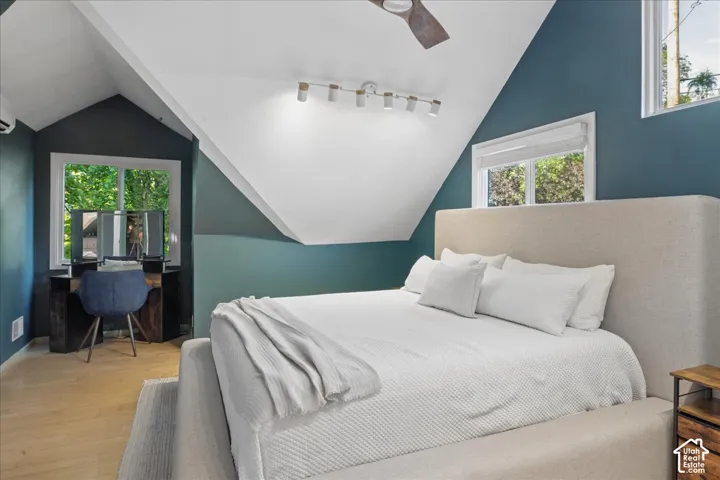 Attic room featuring a sloped ceiling, wood-finish flooring, multiple windows, track lighting and a ceiling fan
