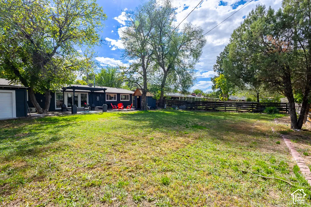 Expansive grassy yard with mature trees, a wood fence, and a patio featuring a pergola