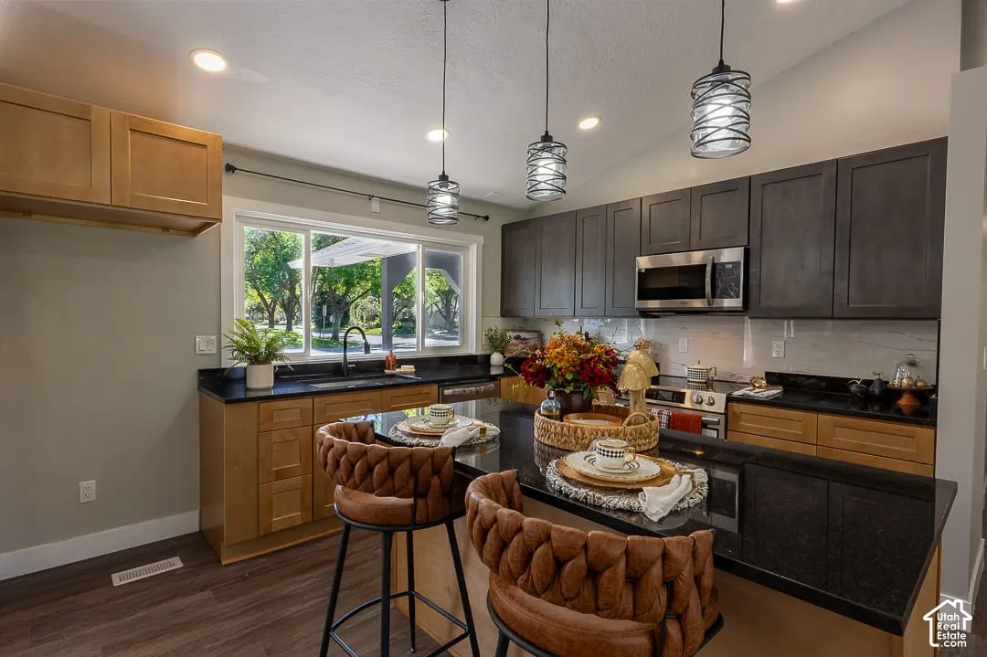 Kitchen featuring wood-finish flooring, dark granite countertops, stainless steel appliances, and a tile backsplash