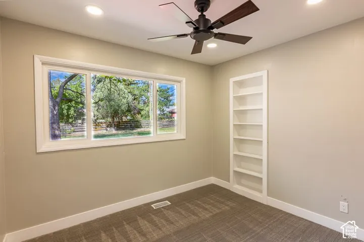 Window with outdoor scenery, ceiling fan with light, recessed lighting, built-in shelving, and carpeting