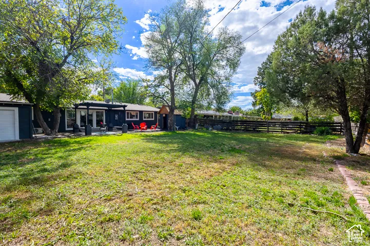 Expansive grassy yard with mature trees, a wood fence, and a patio featuring a pergola