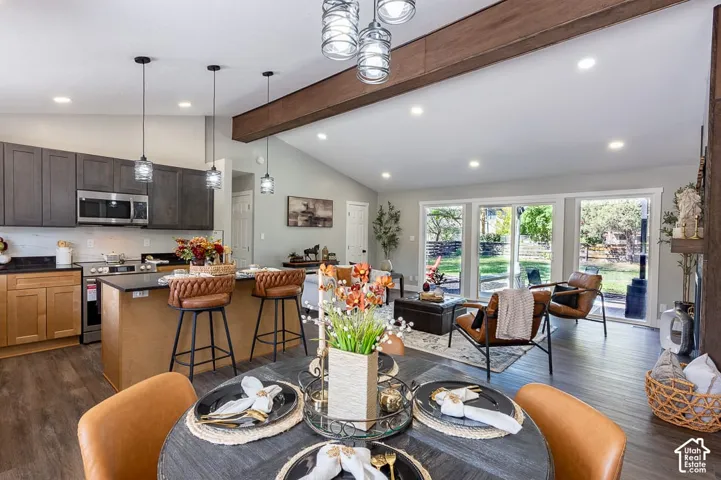 Vaulted ceiling with exposed wood-finish beam, wood-finish flooring, two-tone kitchen cabinetry, stainless steel kitchen appliances, and large sliding glass doors to the exterior