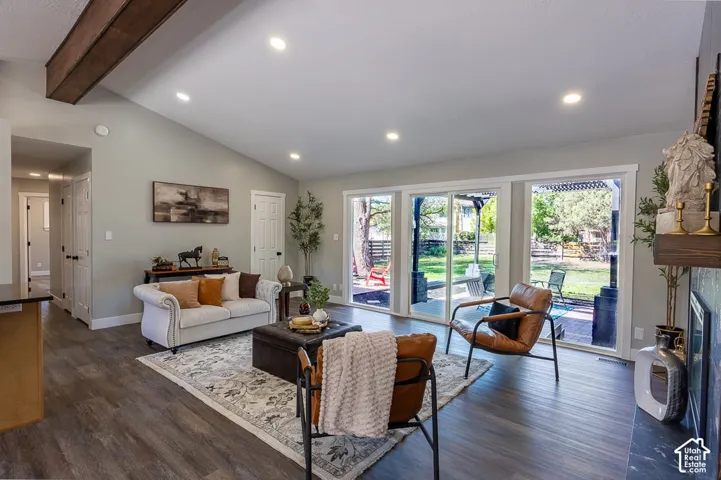 Vaulted ceiling with exposed wood beams, recessed lighting, wood-finish flooring, and multiple glass sliding doors leading to a backyard