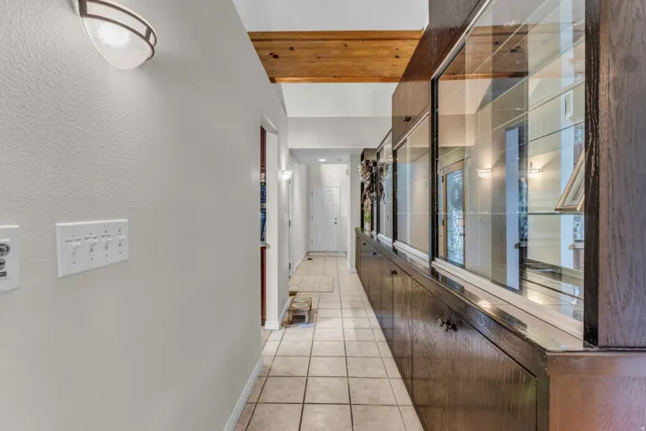 Hallway with tile flooring, built-in display cabinetry with glass fronts, and exposed wood beam ceiling