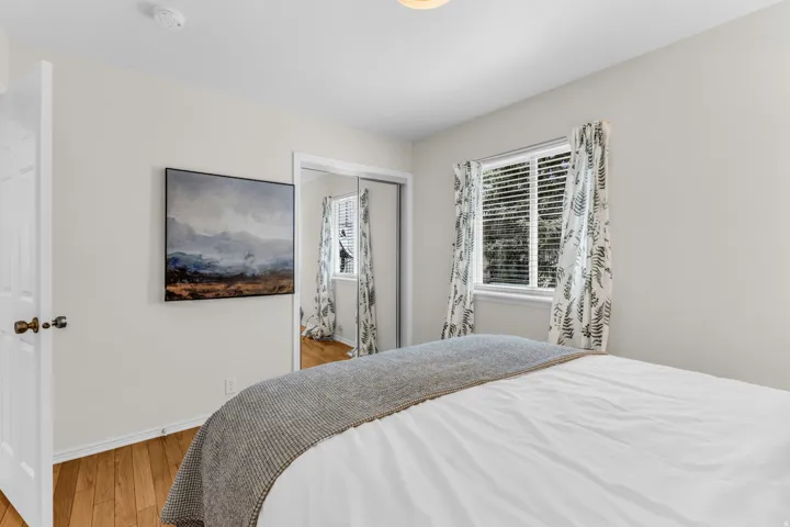 Wood-finish flooring with white trim, a single window with blinds, and mirrored closet doors