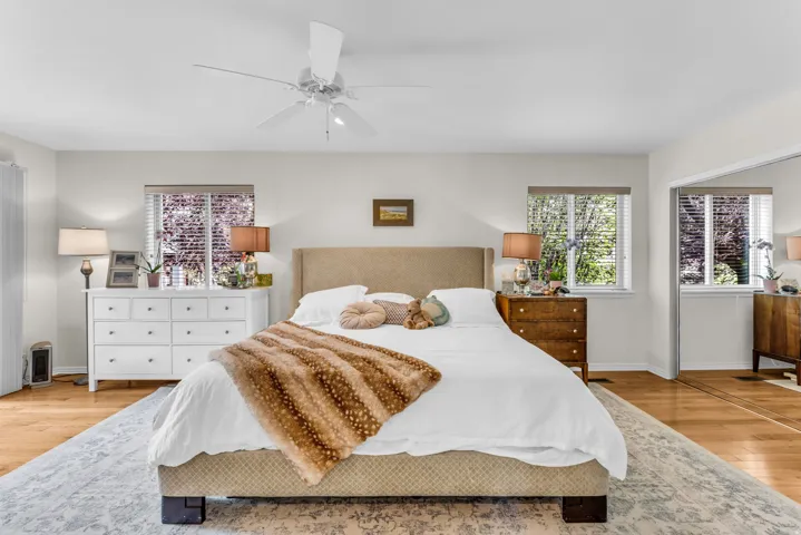 Hardwood flooring, recessed windows with blinds, ceiling fan, and mirrored closet doors