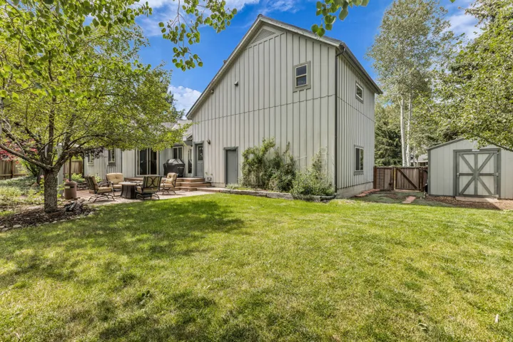 Expansive backyard featuring a large patio, mature trees, a storage shed, and a privacy fence