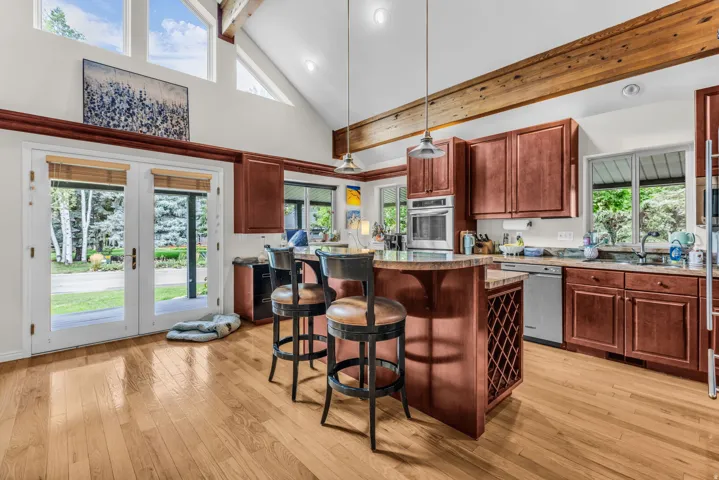 Wood-finish flooring, exposed ceiling beams, cathedral ceiling, white French doors, and built-in wine storage