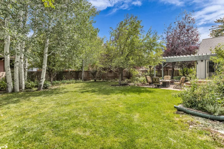 Expansive green lawn with mature trees, stone patio, and a pergola-covered outdoor space