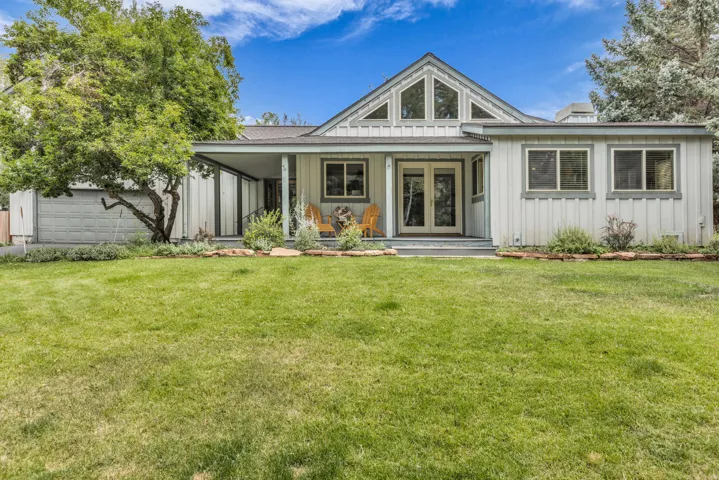 Gabled roofline with large windows, covered porch, board and batten siding, attached garage, and a expansive grassy yard