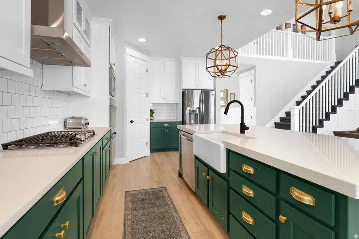 Kitchen featuring green base cabinetry, white upper cabinetry, light-toned countertops, a gas range with a stainless steel hood, and wood-finish flooring