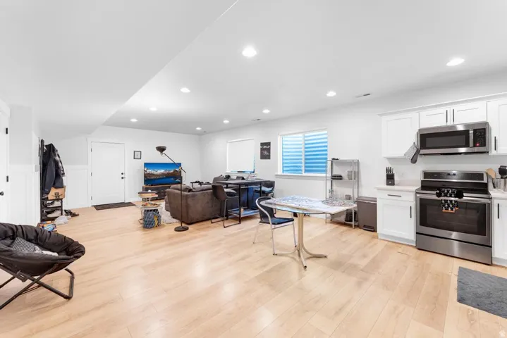 Light wood-finish flooring throughout, white upper and lower cabinetry, stainless steel appliances, recessed lighting, and a white paneled door