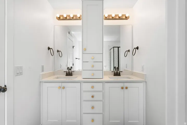 Double vanity with white cabinetry, gold-tone hardware, and light-toned countertops