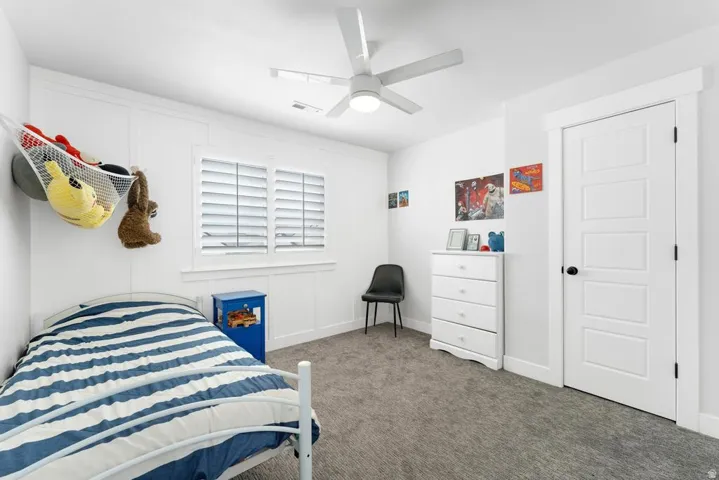 White interior walls, two paneled windows with louvered shutters, ceiling fan with integrated lighting, gray carpet flooring, and a white paneled door