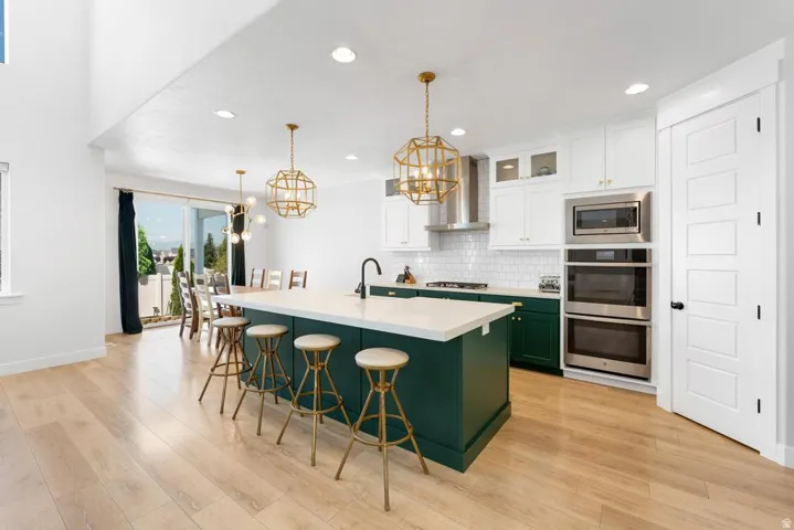 Modern kitchen featuring an expansive center island, light wood-finish flooring, white upper cabinetry, and contrasting deep green lower cabinetry